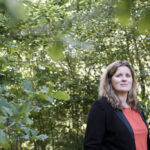 Mandy van Dijk in het groen van nationaal park Dwingelderveld - ze draagt een rood shirt en een zwart colbert